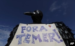 A demonstrator dressed in a black feathered costume holds a sign telling Brazil's President Michel Temer to "get out," during an anti-government protest in Brasilia, Brazil, May 24, 2017.