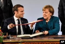 FILE - German chancellor Angela Merkel, right, and French President Emmanuel Macron, left, exchange documents during the signing of the new Germany-France friendship treaty at the historic Town Hall in Aachen, Germany, Jan. 22, 2019.