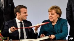 German chancellor Angela Merkel, right, and French President Emmanuel Macron, left, exchange documents during the signing of the new Germany-France friendship treaty at the historic Town Hall in Aachen, Germany, Jan. 22, 2019.