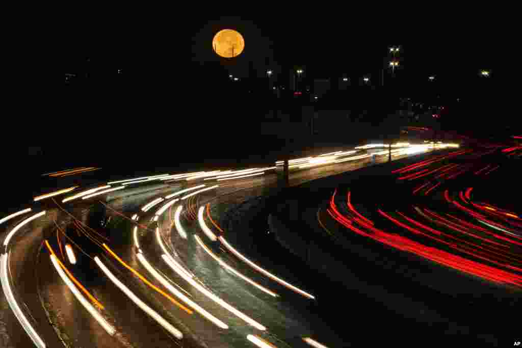 The full moon sets as morning traffic travels on a road in Leawood, Kansas.