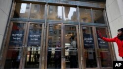 A woman waves from the sidewalk as another locks the front door at Lord & Taylor's Fifth Avenue flagship store which closed for good mid-afternoon, Jan. 2, 2019, in New York. 
