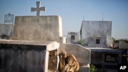FILE - The remains of an exhumed corpse leans against its grave before being taking away to a mass grave in the national cemetery in Port-au-Prince, Haiti, March 29, 2017. Many bereaved Haitians go into a lifetime of debt to send off deceased relatives. Burial costs average $5,000 per household - well over than what most Haitians earn in a year. 
