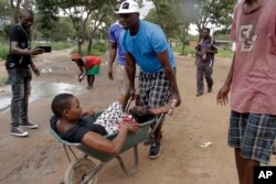 FILE: A woman with a wounded leg during clashes between protestors and police, is transported in a wheelbarrow, during protests over fuel hikes in Harare, Zimbabwe, Monday, Jan. 14, 2019.