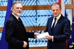 EU Council President Donald Tusk, right, gets British Prime Minister Theresa May's formal notice to leave the bloc under Article 50 of the EU's Lisbon Treaty from UK Permanent Representative to the EU Tim Barrow in Brussels, Wednesday, March 29, 2017.