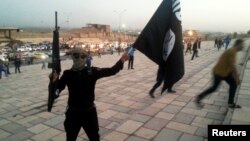 FILE - An Islamic State fighter holds the extremist group's signature flag and a weapon in the Iraqi city Mosul, June 23, 2014. Preparations are underway to wrest the city from IS control.