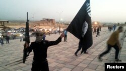 FILE - A fighter of the Islamic State group holds an IS flag and a weapon on a street in the city of Mosul, Iraq, June 23, 2014.