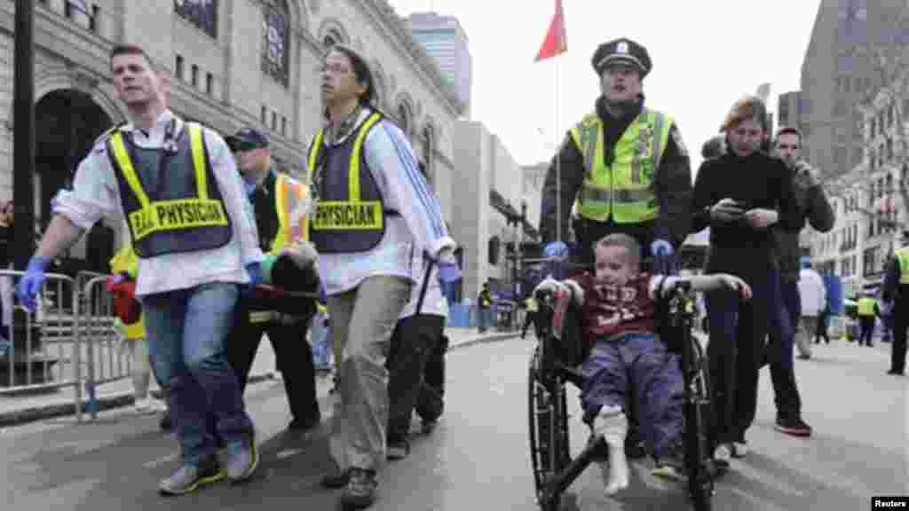 A Boston police officer wheels in injured boy down Boylston Street as medical workers carry an injured runner following an explosion during the 2013 Boston Marathon in Boston, Monday, April 15, 2013.