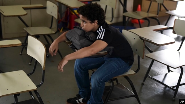 In this Friday, Oct. 13, 2017 photo, a student sits alone in a classroom at Ramon Marin Sola Elementary School, which opened its doors as a daytime community center after the passing of Hurricane Maria in Guaynabo, Puerto Rico. (AP Photo/Carlos Giusti)