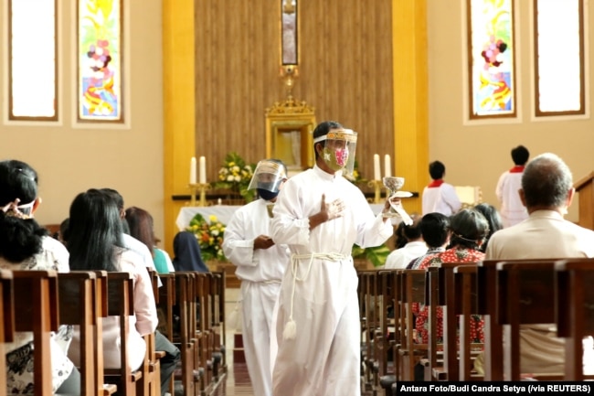 Seorang asisten pastor melayani jemaah saat misa Minggu di sebuah gereja di tengah pandemi COVID di Banyuwangi, Jawa Timur, 14 Juni 2020. (Foto: Antara/Budi Candra Setya via Reuters)