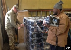 FILE - Staff Sgt. William Phillips, with the Michigan National Guard, assists a resident at a water distribution center at a fire station in Flint, Mich., Jan. 13, 2016.