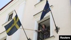 An employee rearranges the national flag of Sweden at the Swedish embassy in Minsk August 8, 2012