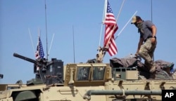 FILE - This April. 29, 2017, still taken from video, shows an American soldier standing on an armored vehicle in the northern village of Darbasiyah, Syria.