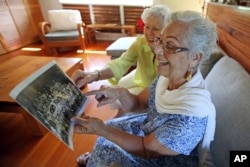Joan Rodby (left) and Emma Veary look at their fifth-grade class photo during a reunion in Makawao, Hawaii.