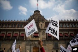 People hold signs reading "Pena out," and "No more gasoline price hikes" as they protest in front of the National Palace in Mexico City, Jan. 1, 2017.