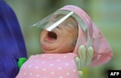 Seorang perawat menggendong bayi yang baru lahir yang dilindungi dengan pelindung wajah di tengah wabah virus corona, di Jakarta, 21 April 2020. (Foto: AFP)