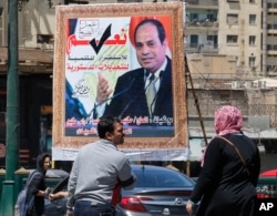 FILE - People walk past a banner supporting proposed amendments to the Egyptian constitution on new term limits, with a poster of Egyptian President Abdel-Fattah el-Sissi in Cairo, Egypt, Apr. 16, 2019.
