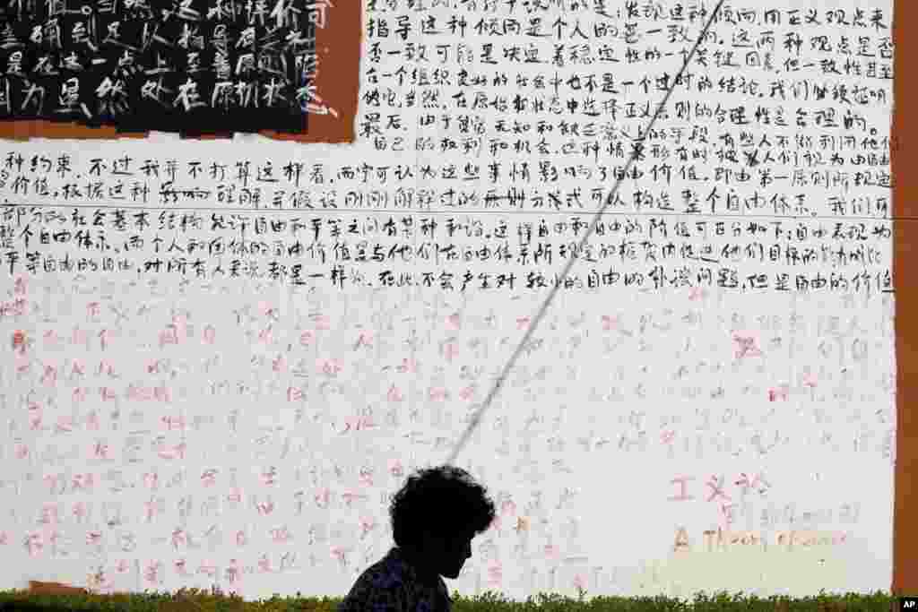 A woman walks past a wall covered with Chinese characters from chapters of John Rawls' book "A Theory of Justice" outside an art gallery in Beijing.