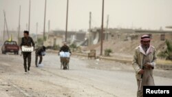 A civilian and fighters from the Syrian Democratic Forces (SDF) walk along a street in the Raqqa's al-Sana'a industrial neighborhood, Syria, June 14, 2017.