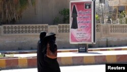 Veiled women walk past a billboard that carries a verse from Koran urging women to wear a hijab in the northern province of Raqqa, March 31, 2014.