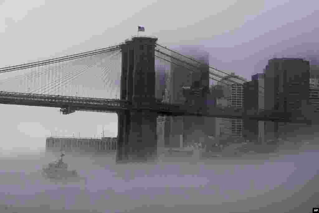 An NYPD boat in enveloped in fog as it patrols the East river under the Brooklyn bridge in New York.