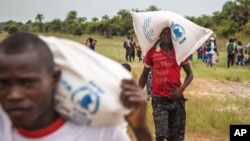 FILE - People carry food aid from a British Navy helicopter after it made a food drop on Sherbro Island, Sierra Leone, Dec. 7, 2014. 