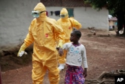 FILE - Health workers accompany a nine-year-old who contracted the Ebola virus to a Monrovia treatment center on Sept. 30, 2014.