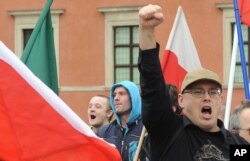 FILE - A supporter of a right wing organization gestures, as others shout slogans during an anti-migrant rally in Warsaw, Poland, Sept. 26, 2015.