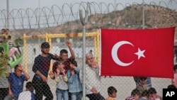 FILE - Migrants stand behind a fence at the Nizip refugee camp in Gaziantep province, southeastern Turkey, April 23, 2016. 