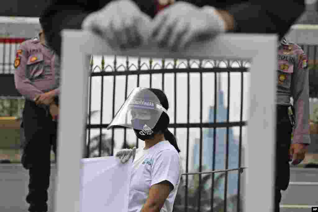 A mirror shows an activist wearing a mask and protective face shield as a measure against the coronavirus outbreak during a small protest outside the parliament in Jakarta, Indonesia.