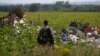 An armed pro-Russian separatist stands guard as OSCE and members of a Malaysian air crash investigation team inspect the crash site of Malaysia Airlines Flight MH17, near the village of Rozsypne, Donetsk region on July 22, 2014.