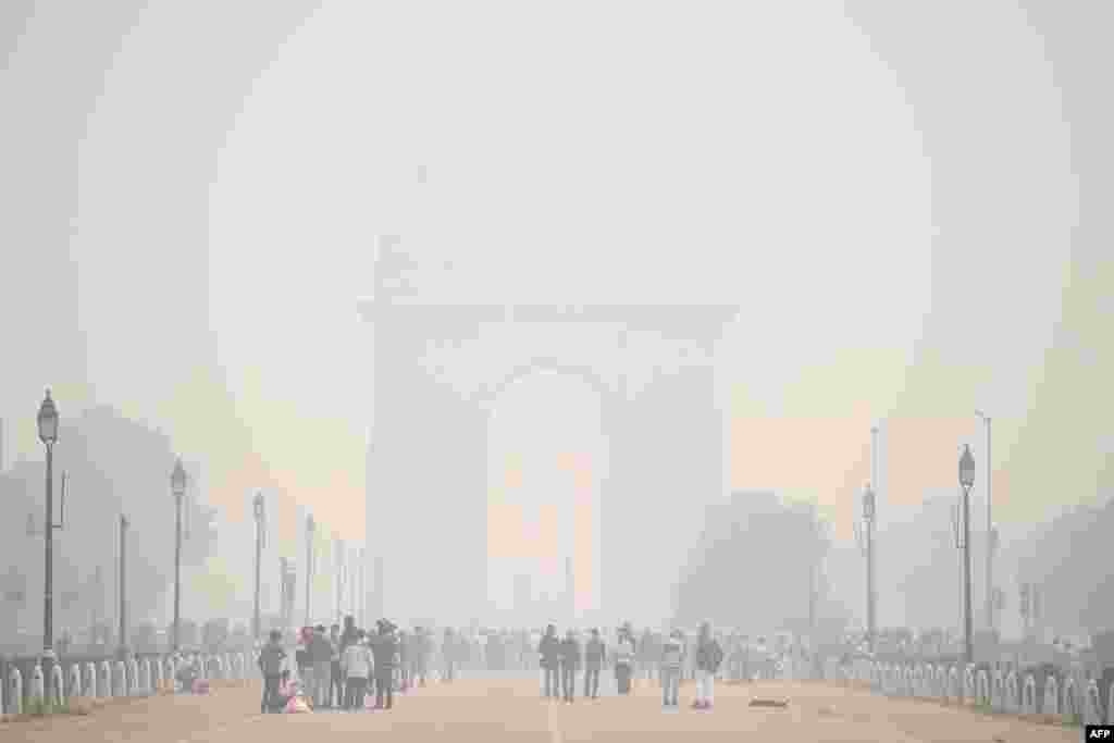 People walk along Rajpath near India Gate under heavy smoke and fog conditions in New Delhi, India.