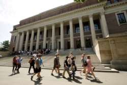 Orang-orang berjalan melewati pintu masuk Perpustakaan Widener, di belakang, di kampus Universitas Harvard, di Cambridge, Massachuset, 16 Juli 2019. (Foto: AP/Steven Senne)