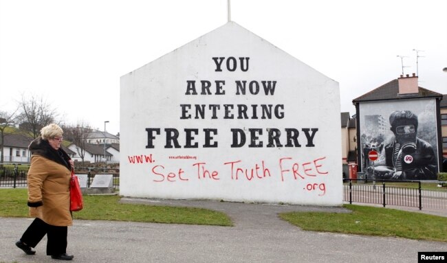FILE - A woman walks past murals in Bogside, Derry, Northern Ireland, March 23, 2010.