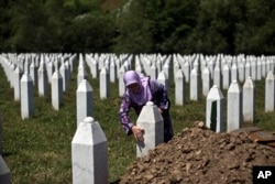 FILE - A woman touches the tombstone of a relative at the Potocari, memorial complex near Srebrenica, 150 kilometers northeast of Sarajevo, Bosnia, July 10, 2015.