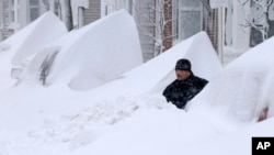 John Silver berusaha membersihkan tumpukan salju yang "mengubur" mobilnya di depan rumahnya di kota Boston, hari Sabtu (9/2). 