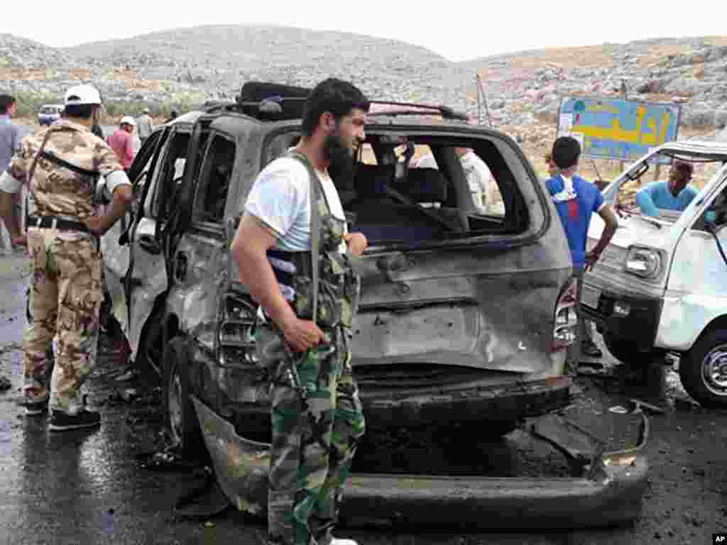 This citizen journalism image provided by Edlib News Network shows Syrian rebels with damaged cars after a car bomb exploded at a crossing point near Syria's border with Turkey, Sept. 17, 2013.