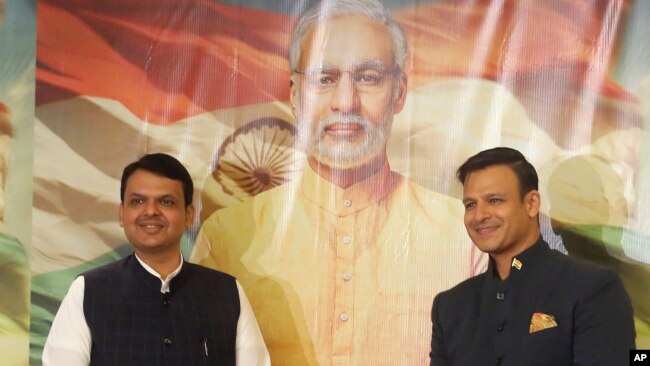 FILE - Maharashtra state Chief Minister Devendra Fadnavis, left, and Bollywood actor Vivek Oberoi stand for a photo in front of a poster for the now delayed film "PM Narendra Modi," in Mumbai, India, Jan. 7, 2019.