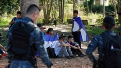 Los inmigrantes hondureños que intentan llegar a Estados Unidos se sientan con sus mochilas y banderas hondureñas cuando son detenidos por la Policía Nacional de Guatemala después de cruzar la frontera hondureña.