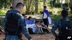 Los inmigrantes hondureños que intentan llegar a Estados Unidos se sientan con sus mochilas y banderas hondureñas cuando son detenidos por la Policía Nacional de Guatemala después de cruzar la frontera hondureña.