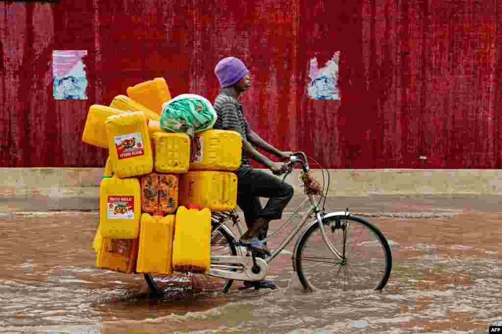A man bicycles down a flooded street with empty cooking oil containers during a rain storm in Dar es Salaam, Tanzania.