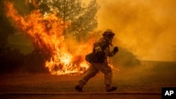 A firefighter runs while trying to save a home as a wildfire tears through Lakeport, Calif., July 31, 2018. 