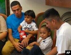 Javier Garrido Martínez, izquierda y Alan García, a la derecha, se sientan con sus hijos de 4 años en una conferencia de prensa en Nueva York, el miércoles 11 de julio de 2018. Los hombres se reunieron con sus hijos después de casi dos meses de haber sido separados por la patrulla fronteriza de EE.UU. al sur del país. Imagen tomada de un video.