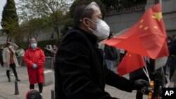 Residents gather outside a park where an official event was held for the national moment of mourning for victims of coronavirus in Wuhan in central China's Hubei Province, Saturday, April 4, 2020. 