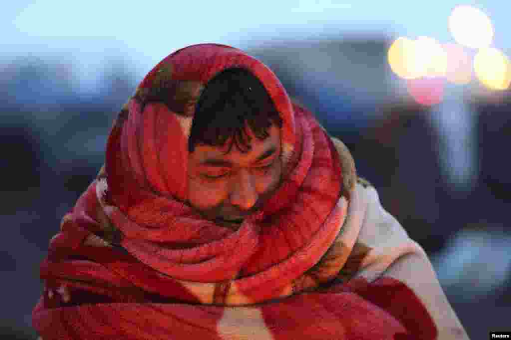 An Afghan immigrant uses a blanket to keep warm near makeshift shelters before he was evacuated by French police from an improvised camp in Calais, northern France.