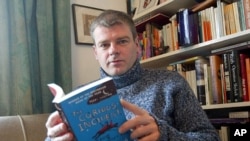 FILE - Mark Haddon, author of "The Curious Incident of the Dog in the Night-Time," poses with a copy of his novel, Oxford, England, March 2004.