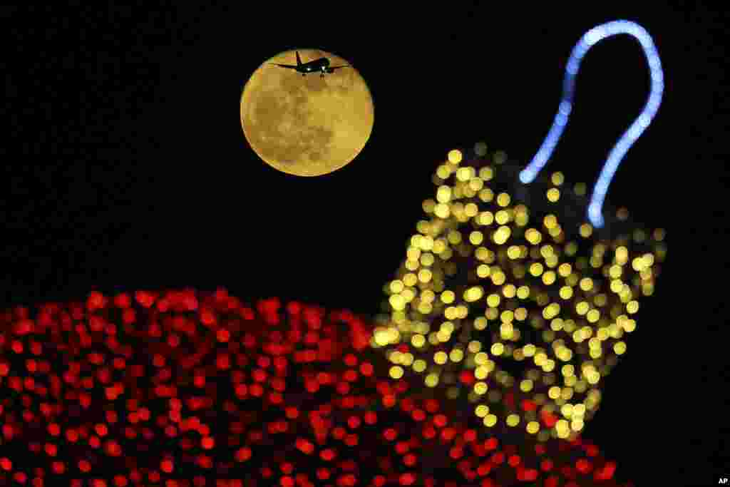 The moon shines behind a decorated with an illuminated Christmas ornament as an aircraft prepares for landing at the airport in southern coastal city of Larnaca In the eastern Mediterranean island of Cyprus, Dec. 23, 2018.