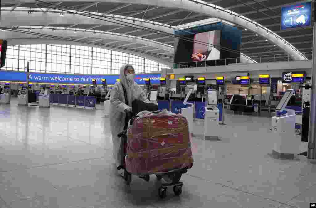 حمل چمدان توسط یک مسافر با لباس محافظتی در فرودگاه هیترو لندن، بریتانیا