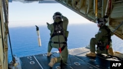 A photo taken on March 20, 2014, shows Royal Australian Air Force Loadmasters, Sergeant Adam Roberts (L) and Flight Sergeant John Mancey (R), preparing to launch a Self Locating Data Marker Buoy from a C-130J Hercules aircraft.