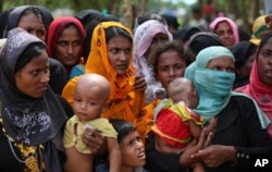 Rohingya women carry children and wait for food handouts at Thangkhali refugee camp in Cox's Bazar, Bangladesh, Oct. 5, 2017.