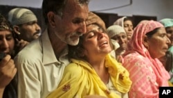 A Pakistani man comforts his relative mourning the death of a family member killed in gas cylinder explosion on a minibus, in Gujrat, Pakistan, May 25, 2013.